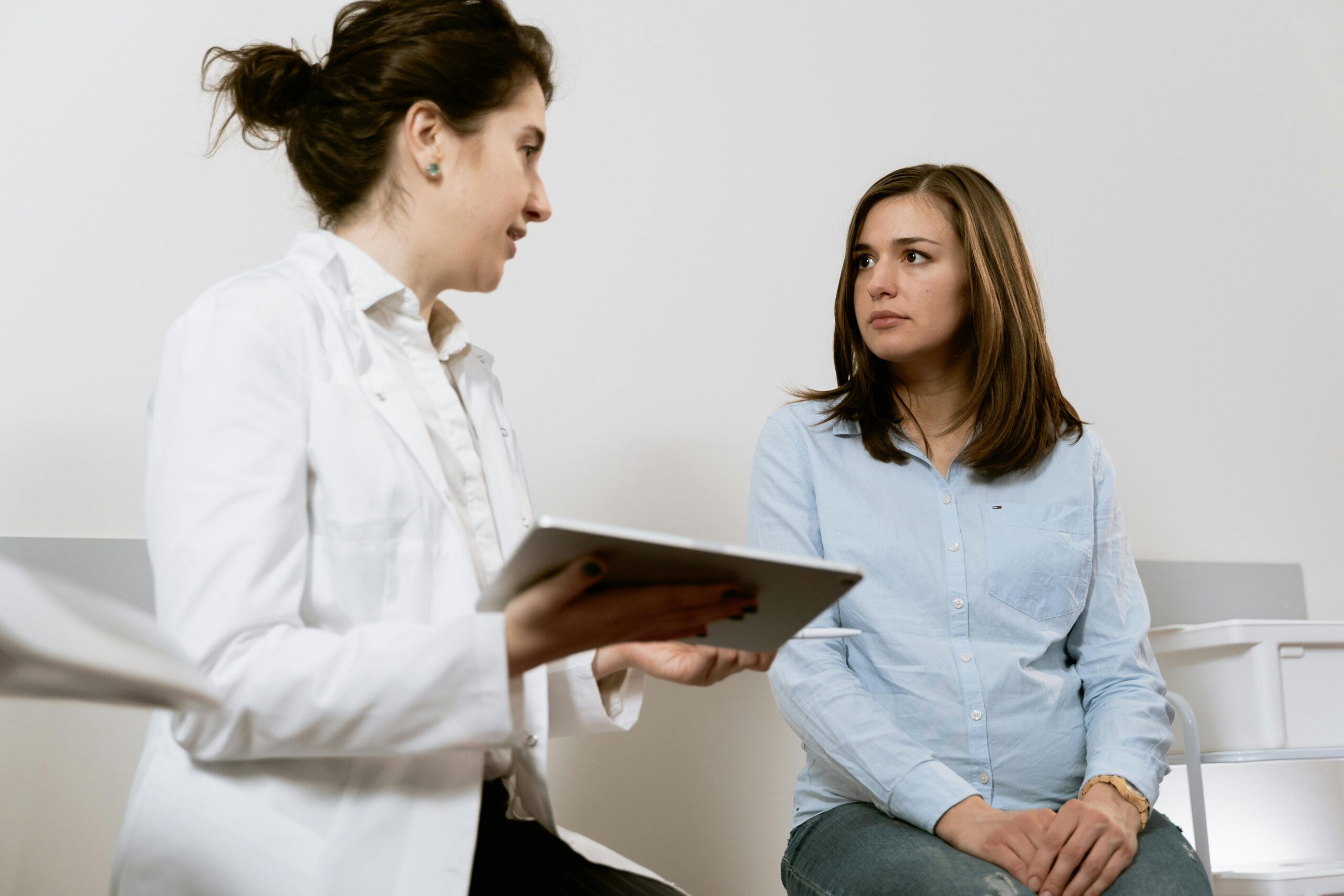 a woman in a white coat holding a tablet and looking at another woman